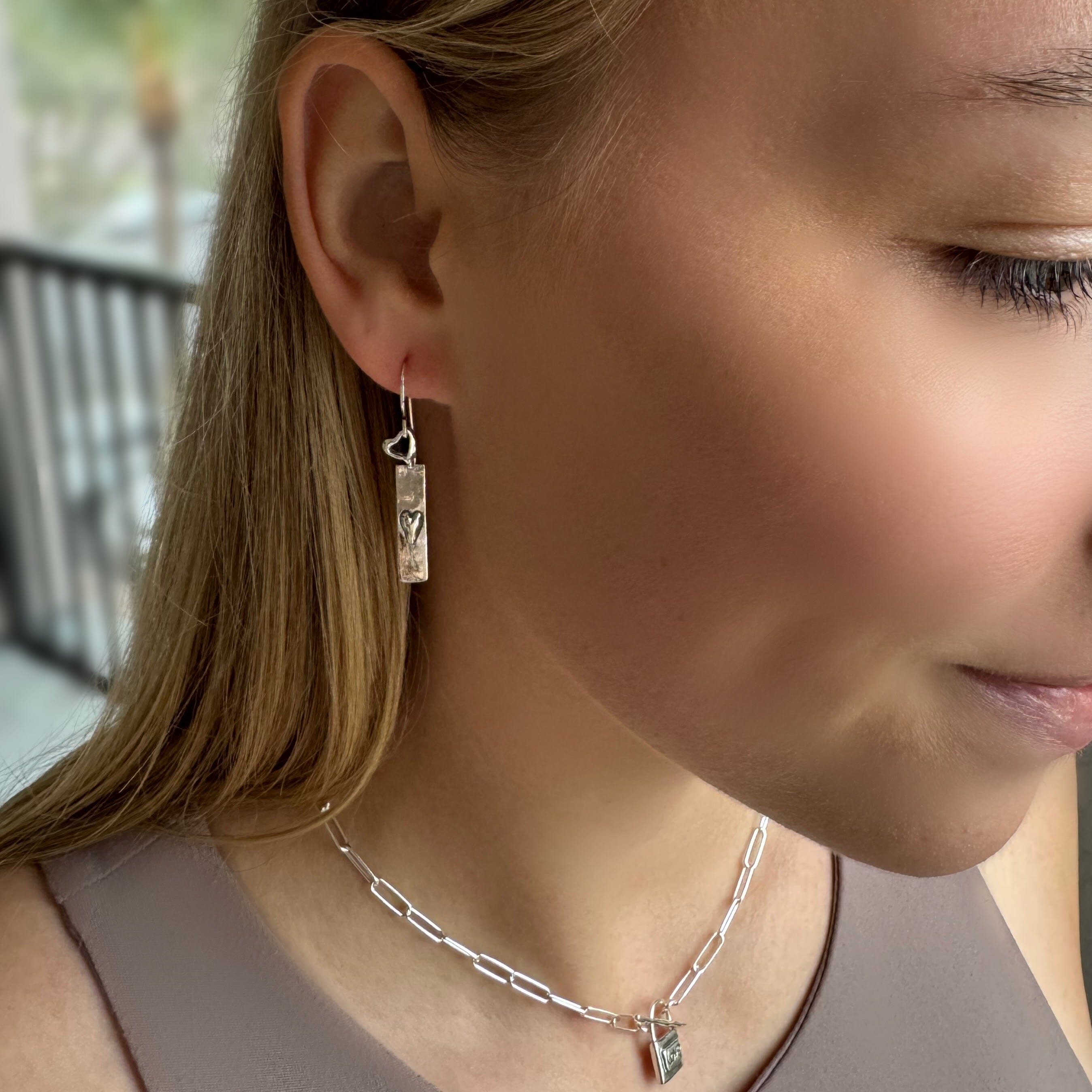 sterling silver earrings with a heart cutout at the top and a raised heart on the pendent